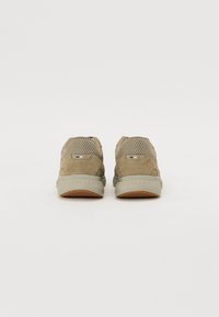 Adidași din suede bej cu accente din plasă, talpă din cauciuc, guler căptușit și design minimalist. Vederea din spate arată contrastul materialelor în două tonuri.