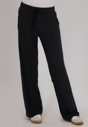 Zwarte broek met elastische tailleband en trekkoord, met een ontspannen pasvorm en lichte stof, gecombineerd met witte sneakers met gumrubberen zolen.