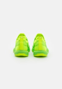 Neonowe zielone buty sportowe z teksturowaną siateczką, wyściełanym kołnierzem i wyraźną pętelką na pięcie. Na tyle znajduje się odważny napis "TRENING".