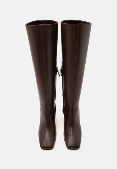 Paire de bottes hautes en cuir marron foncé avec talons carrés et fermetures éclair latérales, debout sur un fond clair uni.
