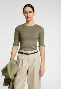 Olivnozeleni rebrasti pleteni top s kratkimi rokavi in okroglim izrezom, v kombinaciji s svetlo bež hlačami visoko pasu in ustreznim zelenim blazerjem.