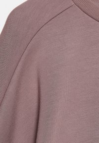 Tessuto di felpa rosa polveroso con una texture morbida, colletto a coste e spalle leggermente scese. La vista ravvicinata mette in evidenza la trama del materiale.