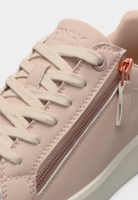 Ανοιχτό ροζ αθλητικό παπούτσι με κρεμ κορδόνια και διακοσμητικό ροζ χρυσό φερμουάρ κατά μήκος της πλευράς, με διακριτικό ανάγλυφο όνομα της μάρκας στη γλώσσα.