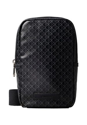 Melnā Calvin Klein pleca soma ar diagonālu ģeometrisku rakstu un rāvējslēdzēja aizdari, ar auduma siksnu un logotipa uzlīmi.