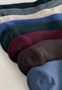 Calze piegate assortite in blu scuro, marrone, bordeaux, verde, blu royal, beige, grigio e navy, disposte sovrapposte su una superficie chiara.