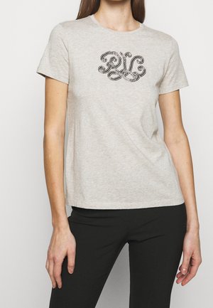 T-shirt gris clair à manches courtes en tissu doux, avec un motif brodé foncé sur la poitrine rappelant des lignes et courbes fluides.