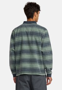 Gestreiftes Langarmhemd in Grün und Marineblau mit einer lockeren Passform, featuring einen Kragen, geknöpften Ärmeln und einem abgerundeten Saum. Texturiert.