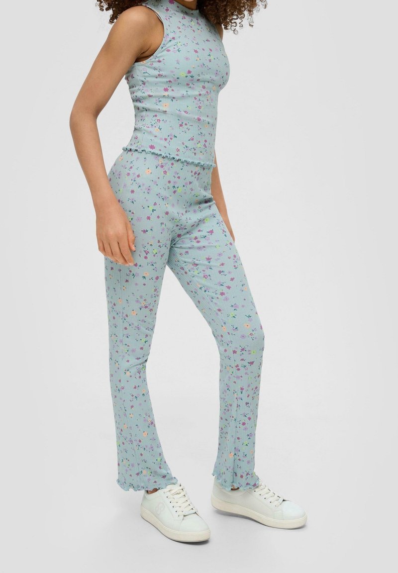 Femme portant un haut sans manches côtelé bleu clair et un pantalon évasé assorti avec un petit imprimé floral multicolore et des baskets blanches.
