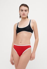 Fekete bikinitop fehér csíkkal és téglalap alakban, piros bordás bikinitangával, fehér részletekkel párosítva.