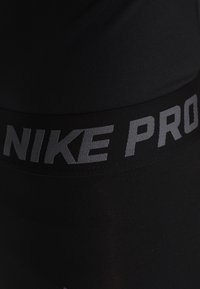 Leggings sportivi neri con una texture liscia, dotati di una cintura elastica ampia etichettata "NIKE PRO" in lettere grigie.