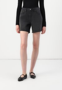 Zwarte denimbroekshorts met een hoge taille, voorzakken en een knoopsluiting. Soepele textuur met een licht vervaagde afwerking. Platte zwarte schoenen met accenten.