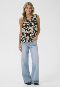 Top floral sans manches en noir et crème, avec un décolleté en V et un détail à nouer. Associé à un jean large bleu clair et des chaussures noires.