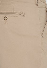 Beige tyg med en knäppt bakficka och sydda detaljer på skräddarsydda byxor eller shorts.