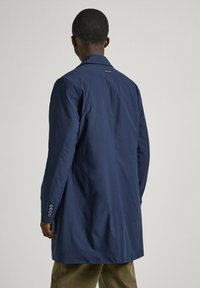 Jūras kara flotes garais mētelis, kas izgatavots no gludas auduma, ar izsmalcinātu dizainu, vienu aizmugurējo ventilu un pogu aksesuāriem uz piedurknēm, skatoties no aizmugures.