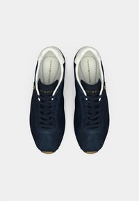 Σκούρα μπλε σουέντ αθλητικά παπούτσια με λευκές λεπτομέρειες και χρυσό λογότυπο. Διαθέτουν στρογγυλεμένη μύτη, επίπεδα κορδόνια και υφασμένο καουτσούκ στην εξωτερική σόλα.