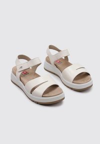 Sandalias de cuero blancas con una correa ajustable, puntera abierta y una plantilla acolchada. Suela gruesa blanca y marrón con diseño troquelado.