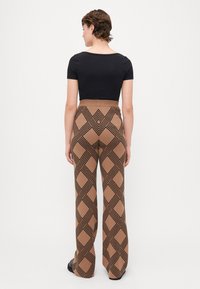 Bruine wijde broek met een geometrisch zwart en tan ontwerp, gecombineerd met een getailleerd zwart T-shirt met korte mouwen, gezien van achteren.