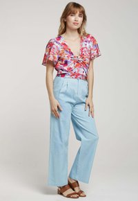 Haut à imprimé floral avec des manches courtes, décolleté en V profond, détail noué ; pantalon large taille haute bleu clair ; sandales à lanières marron.