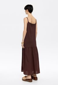 Abito maxi marrone con spalline sottili, corpino texturizzato e orlo a volant. Tessuto morbido, design a strati e vestibilità rilassata.