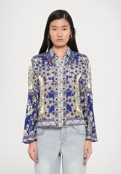 Blouse à motifs floraux en bleu, blanc et or avec des manches longues et un col. Tissu léger avec des éléments de design détaillés.