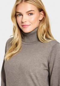 Maglione dolcevita marrone realizzato in materiale a coste, con maniche lunghe e design aderente. Texture liscia con dettagli di cucitura discreti.