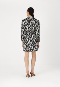 Schwarz-weiß gemustertes Kleid mit langen Ärmeln, tailliertem Schnitt und kurzer Länge, ergänzt durch braune High-Heelsandalen.