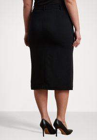 Μαύρη μολυβένια φούστα από λείο ύφασμα, με εφαρμοστή σιλουέτα, πίσω άνοιγμα και διακριτική ζώνη. Συμπληρώνεται από μαύρες ψηλές γόβες.