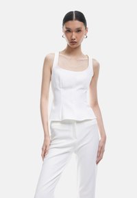 Witte aangesloten top met een vierkante halslijn en brede schouders, met een peplum onderkant. Gladde textuur, minimalistisch ontwerp, gecombineerd met witte broeken.