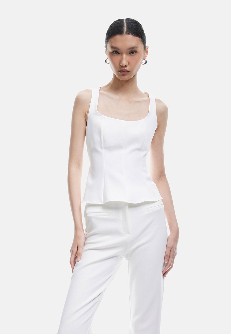 Witte aangesloten top met een vierkante halslijn en brede schouders, met een peplum onderkant. Gladde textuur, minimalistisch ontwerp, gecombineerd met witte broeken.