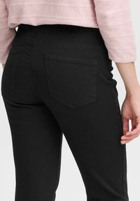Zwarte denim jeans met een slim fit snit, voorzien van twee achterzakken met stikdetails en een soepele textuur. Gekocht met een lichtroze top.