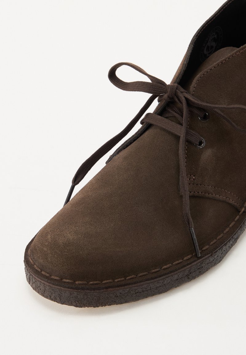 Bruine suède veterschoen met een ronde neus, een gestructureerde bovenkant en een contrasterende donkere zool, voorzien van bruine veters en minimale stikseldetails.