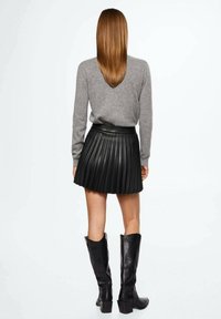 Un pull gris, une jupe plissée en cuir noir et des bottes noires jusqu'aux genoux. La jupe a une taille ajustée et une texture superposée.