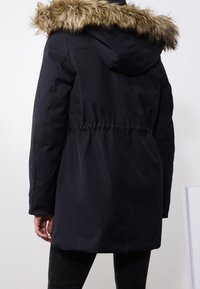 Czarna parka z kapturem wykończonym sztucznym futrem, taliowana, z długimi rękawami i gładkim wykończeniem. Charakteryzuje się średnią długością i minimalistycznym designem.