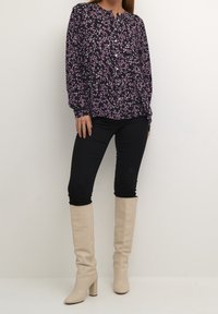 Langærmet skjorte med knapper i mørkeblå med pink blomster mønster. Sættes sammen med sorte skinny jeans og knæhøje beige hæle støvler.