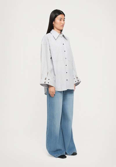 Oversized gray and white striped button-up shirt with a large collar, featuring black buttons and wide cuffs, paired with light blue wide-leg jeans.