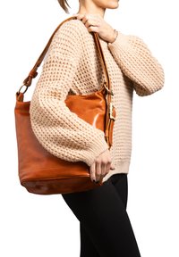 Borsa a spalla in pelle morbida color tan, forma a secchiello con corpo strutturato, dotata di manico staccabile e dettagli in metallo dorato.