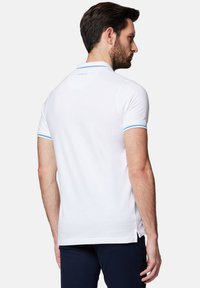Biała koszulka polo z niebieskimi paskami akcentującymi na kołnierzyku i rękawach, wykonana z gładkiego materiału, z bocznym rozcięciem dla większego komfortu.