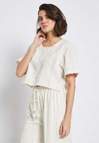 Häkel-Top und Hose mit Kordelzugset in Off-White. Strukturiertes Gewebe mit ausgefransten Kanten und lockerer Passform. Lässiges und atmungsaktives Design.