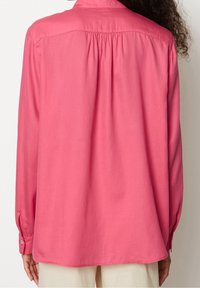 Camicia a maniche lunghe con bottoni di un vivace rosa, caratterizzata da una vestibilità comoda con pieghe sul retro e polsini con bottoni. Tessuto dalla consistenza liscia.