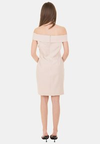 Abito beige a spalle scoperte realizzato in un tessuto strutturato, con una silhouette aderente e una cerniera centrale sul retro. La lunghezza è a metà coscia.