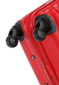 Valise rouge avec surface texturée, dotée de roues noires lisses et pivotantes ainsi que d'une fermeture éclair robuste. Quincaillerie accentuée en métal visible.