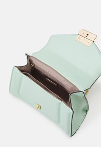 Mintgrön läderhandväska med en guldfärgad lås, öppen för att avslöja ett taupe-färgat tyginteriör och ett zip-ficka.