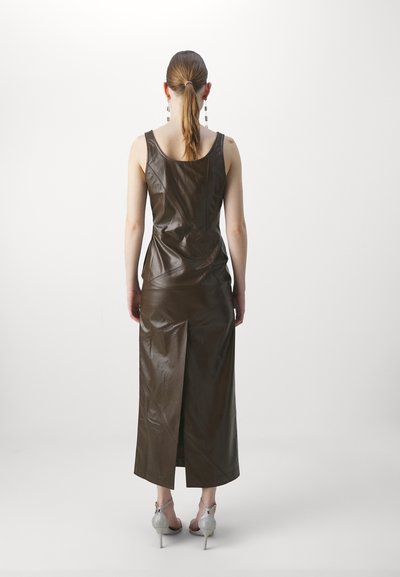 Rochie din piele maro, fără mâneci, cu decolteu rotund, corset ajustat și fente la spate. Asortată cu tocuri argintii cu bretele, design minimalist.