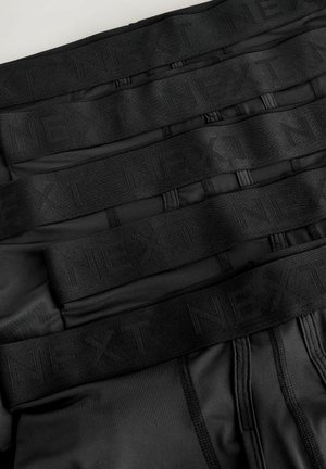 Crne bokserice složene uredno, s širokim crnim elastičnim remenom na kojem je utisnut natpis "NEXT". Glatka tkanina s minimalnim detaljima šivanja.