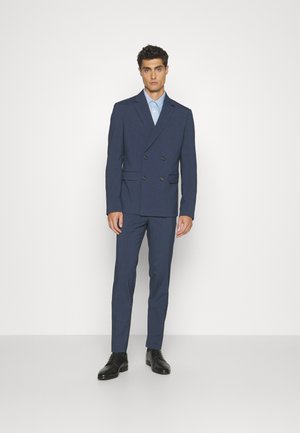 Navy blue double-breasted suit with notched lapels, button details, slim-fit trousers, paired with a light blue shirt and black dress shoes.