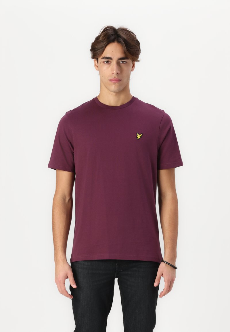 T-shirt à manches courtes de couleur bordeaux en coton doux, avec un col rond et un petit logo jaune sur la poitrine gauch.