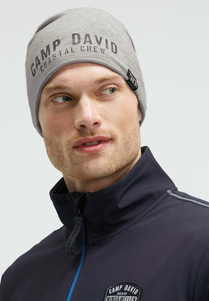 Gray knit beanie featuring "CAMP DAVID COASTAL CREW" in black print. Stitched tag on the side. Worn with a dark navy zip-up jacket.