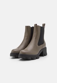 Par de botas de tobillo de cuero topo con suelas de lug negras gruesas y paneles laterales elásticos, fotografiadas sobre un fondo blanco.