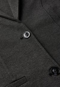 Ciemnoszary żakiet o fakturowanej tkaninie. Posiada klapę w stylu notched oraz dwa czarne guziki z dekoracyjnym grawerunkiem.