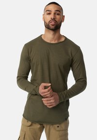 Langærmet olivengrøn skjorte med rund halsudskæring og blød tekstur, designet med en tætsiddende silhuet og en let flosset kant.
